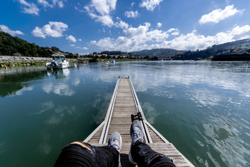 persona sentada en un puerto con un lago o rió de fondo, cielo despejado