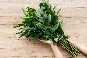 Cropped view of florist holding green bouquet on wooden surface