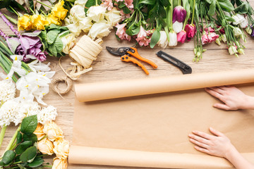 Cropped view of florist with craft paper and colorful flowers on wooden surface
