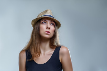 Beautiful young woman in hat and black shirt is looking up isolated on gray background in a studio close up