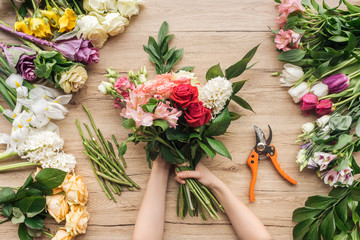 Cropped view of florist holding flower bouquet on wooden table