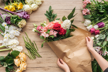 Cropped view of florist making flower bouquet on wooden surface