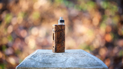 high end natural stabilized wood box mods with rebuildable dripping atomizer on bokeh texture background, vaping device, selective focus