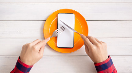 Man eating blank smartphone with knife and fork