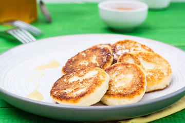 Close-up of homemade cottage cheese pancakes with honey on a plate on a wooden table