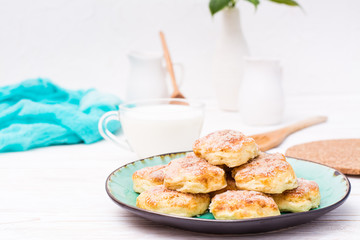 Cottage cheese cookies sprinkled with sugar on a plate and a cup of milk on a wooden table