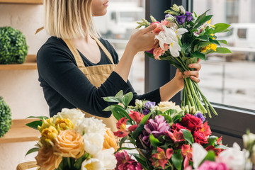 Cropped view of florist in apron holding bouquet in flower shop - obrazy, fototapety, plakaty