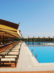 Woman in a straw hat relaxing on a daybed near a luxurious summer pool, concept time to travel.