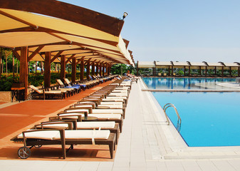 Woman in a straw hat relaxing on a daybed near a luxurious summer pool, concept time to travel.
