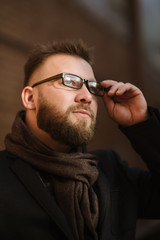 A man with a beard in a black warm coat with a scarf poses to advertise men's clothing in the winter. Advertise men's clothing