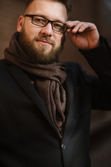 Obraz premium A man with a beard in a black warm coat with a scarf poses to advertise men's clothing in the winter. Advertise men's clothing