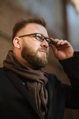 A man with a beard in a black warm coat with a scarf poses to advertise men's clothing in the winter. Advertise men's clothing