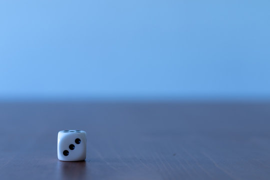 Single white dice on a table with 3 dots on the front side