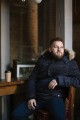 Fototapeta premium A man with a beard in a warm winter jacket poses for advertising men's clothing in the winter. Advertising of men's clothing