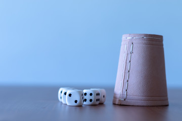 Brown leather yahtzee cup beside some white dices on wooden table