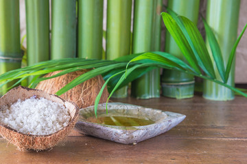 Fototapeta na wymiar Spa or body care concept: sea salt in the coconut, massaging oil, palm leaf and bamboo trunk on old wooden background