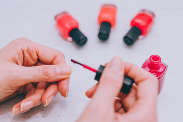 woman's hands with red nail polish bottle and other colors on wooden surface