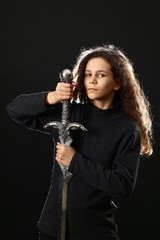 Emotional portrait of a girl with long curly hair with a sword on a black background,