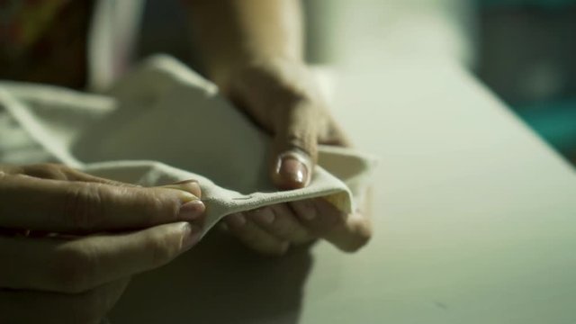Close up of asian hand seamstress sewing a white clothes. Female seamer uses needle and thread by hand according to the ancient tradition. Slow motion shot in low light in vintage style.