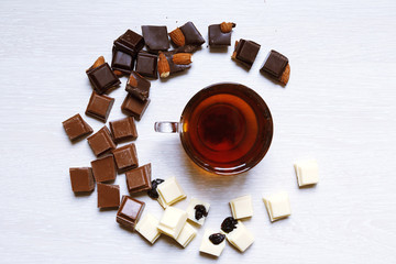 A cup of tea is surrounded by pieces of white, milk and black chocolate.