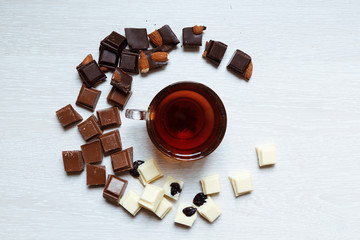 A cup of tea is surrounded by pieces of white, milk and black chocolate.