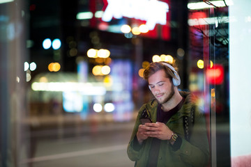 Young man using smartphone on urban street at night