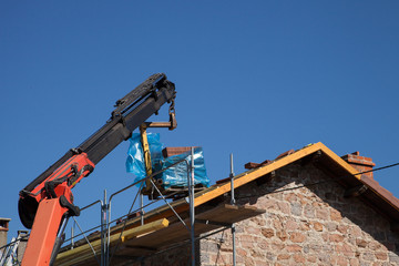 Bras de grue transportant une palette de tuiles pour la r&eacute;novation du toit d'une maison