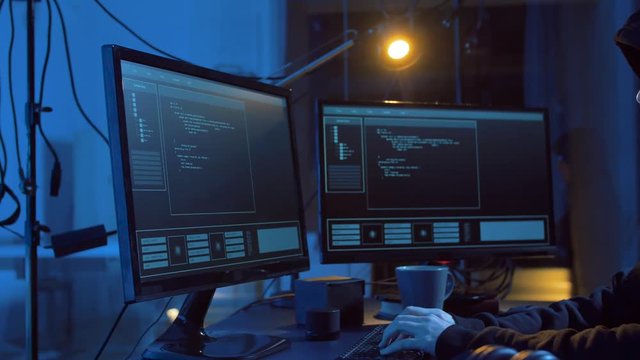 cybercrime, hacking and technology concept - male hacker in dark room creating code or using computer virus program for cyber attack