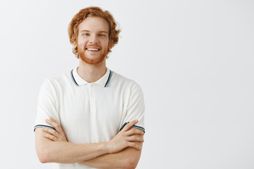 Indoor shot of friendly and carefree happy redhead guy with wavy hair in white polo shirt holding...