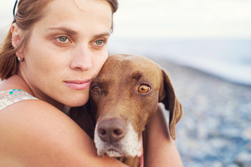 Young girl embraces a sad brown dog on the seashore, soft focus	