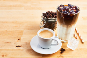 Cup of coffee or espresso, iced coffee and latte macchiato in tall glass with straws on wooden table. Various types of coffee. Copy space for text.