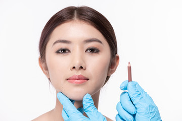 Surgery concept. The doctor is drawing a pencil on the patient's face. The patient is confident in...