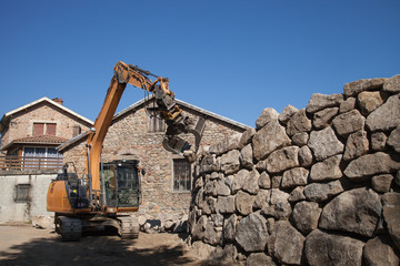 Une pelle mécanique va déposer une lourde pierre au sommet d'un mur de soutènement en construction