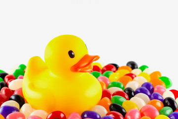 Close up of a toy rubber duck surrounded by jelly beans against a white background.  Landscape cropped. Copy space above.