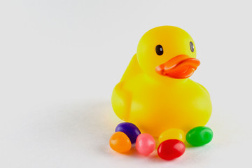 Close up of a toy rubber duck with a few jelly beans in front.  Isolated on white.  Copy space on the left.