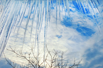 Big icicles under the roof against the background of a cloud sky.