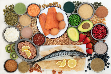 Body building health food with high protein fish, dairy, nuts, seeds, legumes, grains, dietary supplement powders and tablets, vegetables and fruit. Top view on white wood.  