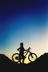 Silhouette of a little girl with a bicycle at sunset