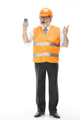 The builder in a construction vest and an orange helmet talking on a mobile phone about something. Safety specialist, engineer, industry, architecture, manager, occupation, businessman, job concept