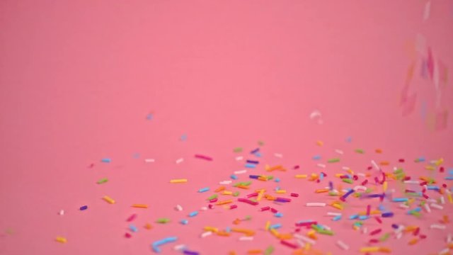 colorful sprinkles falling on pink background, decoration for cake and bakery, slow motion