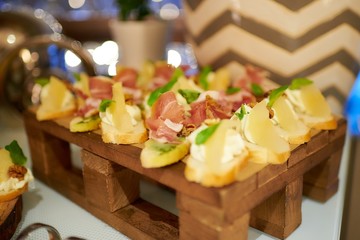 A lot of different snacks with pork and pineapple on a small wooden pallet in a restaurant. An amazing bokeh on the background.