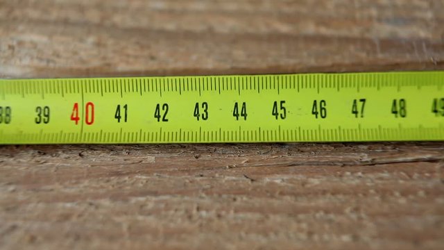The carpenter measures the length of the board with a metal tape measure.
