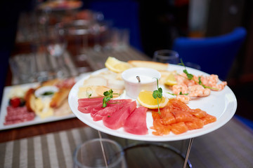 Round plate with shrimps, lemon, herbs, slices of redfish, whitefish, tuna in a nightclub. 