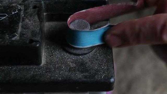 The driver cleans the battery terminals from oxidation with emery paper.