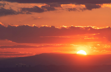 The golden hour of sunset. Orange sky with clouds and yellow sun shining over the mountains.