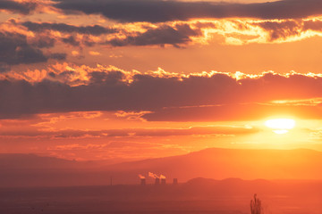 The golden hour of sunset. Orange sky with clouds and yellow sun shining over the mountains.