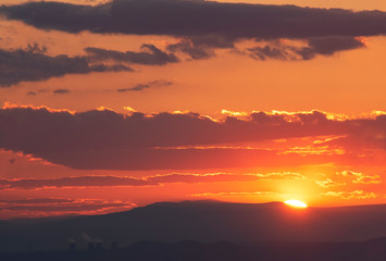 The golden hour of sunset. Orange sky with clouds and yellow sun shining over the mountains.