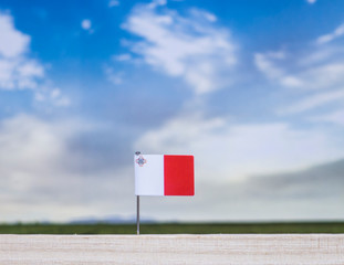 Flag of Malta with vast meadow and blue sky behind it.