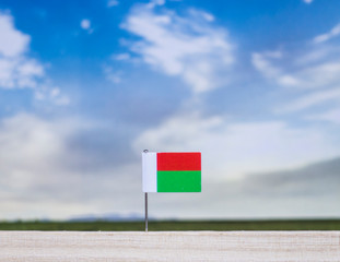 Flag of Madagascar with vast meadow and blue sky behind it.