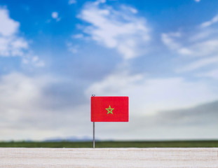 Flag of Morocco with vast meadow and blue sky behind it.